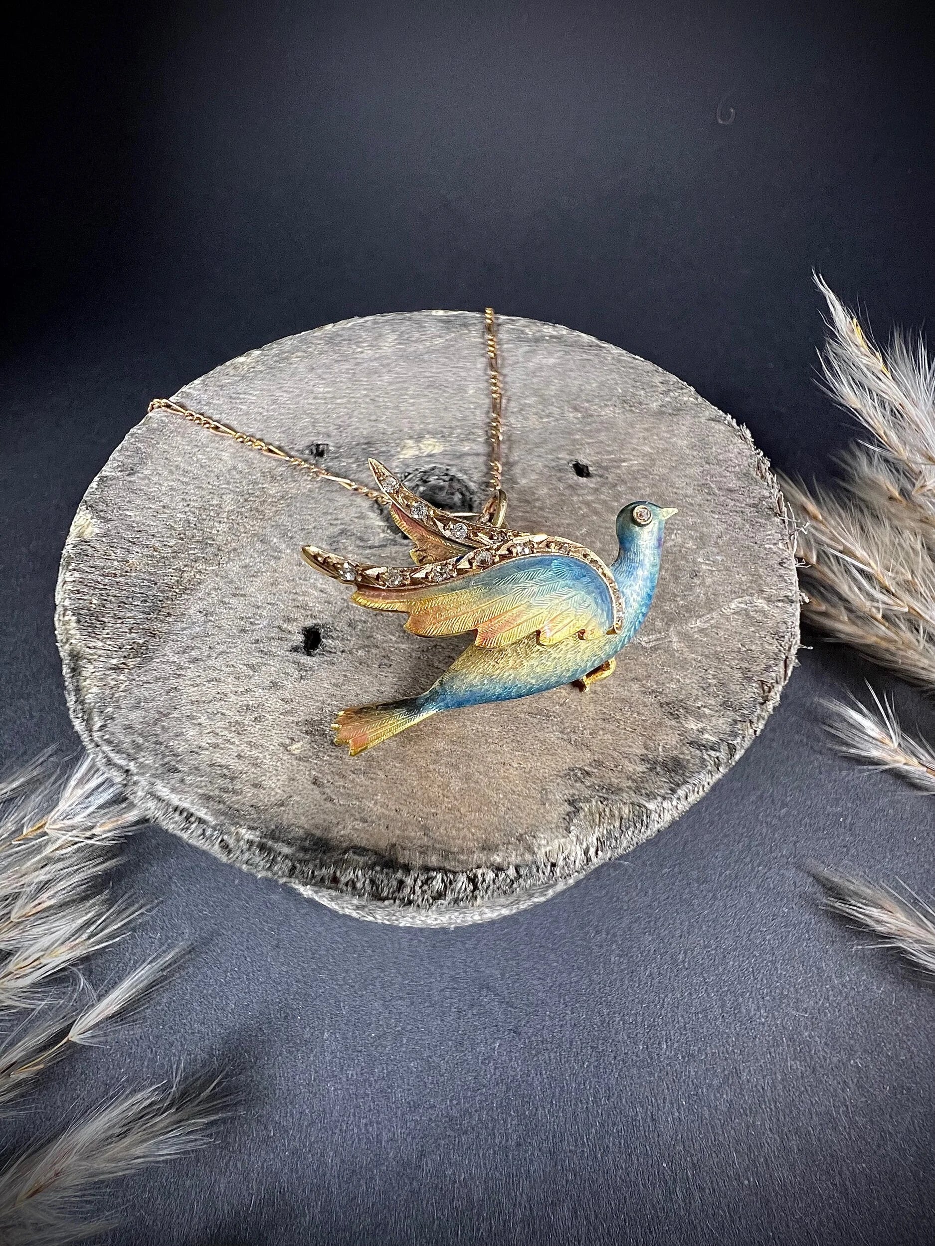 An enamel and diamond dove bird pendant, with a chain, on a wooden spool