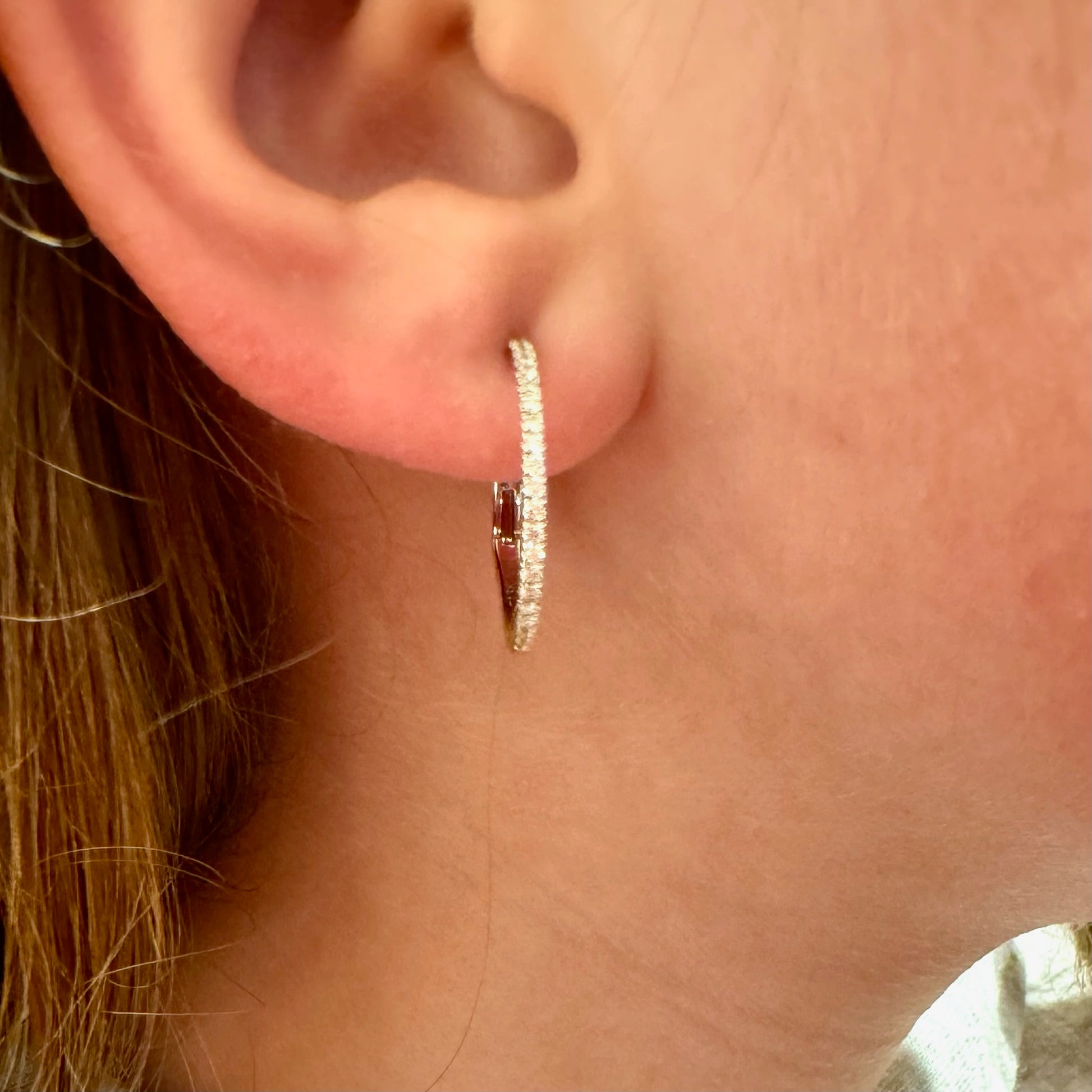 A white gold diamond hoop earring, modelled in an ear