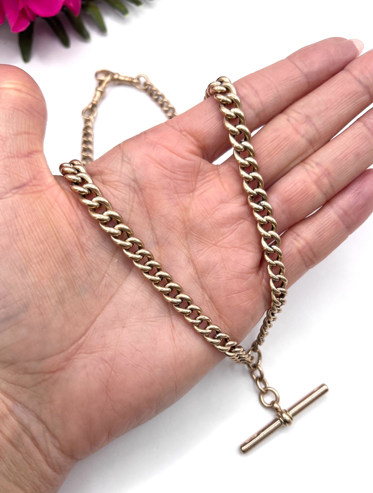A rose gold curb link Albert chain with t-bar, held in a hand