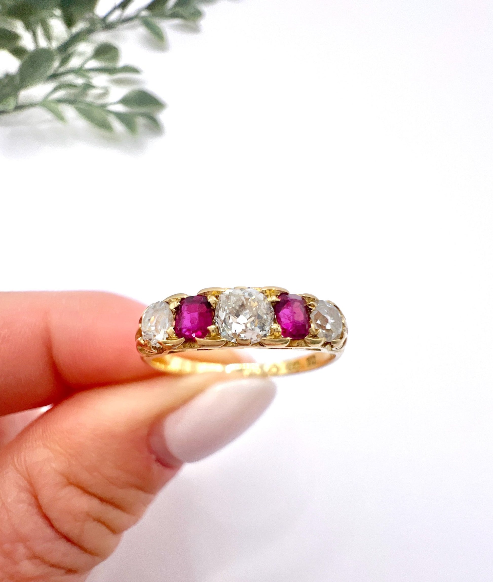 A yellow gold ruby and diamond five stone ring, held in a hand