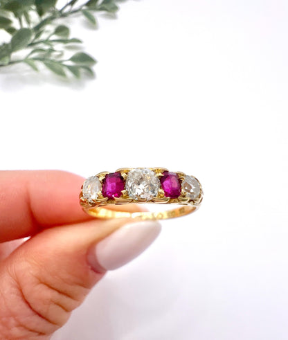 A yellow gold ruby and diamond five stone ring, held in a hand