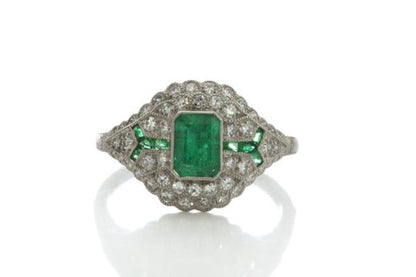 Art Deco Style Emerald, Diamond and Platinum Cluster Dress Ring; central emerald-cut emerald surrounded by brilliant-cut diamonds and accented by calibre-cut emerald set shoulders. Circa 1980s