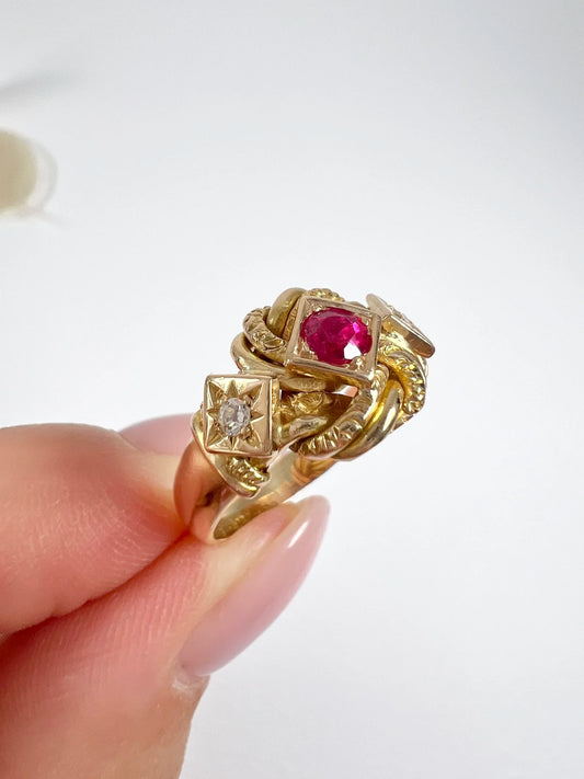 A yellow gold ruby and diamond three stone knot ring, held in a hand
