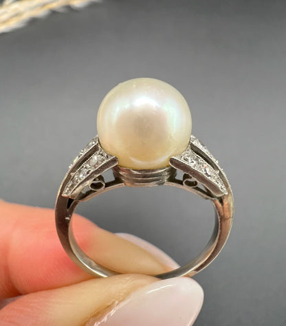 A pearl and diamond ring in platinum, held in a hand