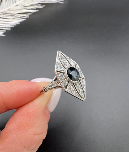 A navette shaped cluster cocktail ring with a sapphire centre surrounded by diamonds, in platinum, held in a hand