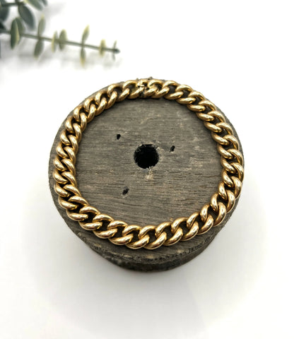 A curb link bracelet in yellow gold, on a wooden spool