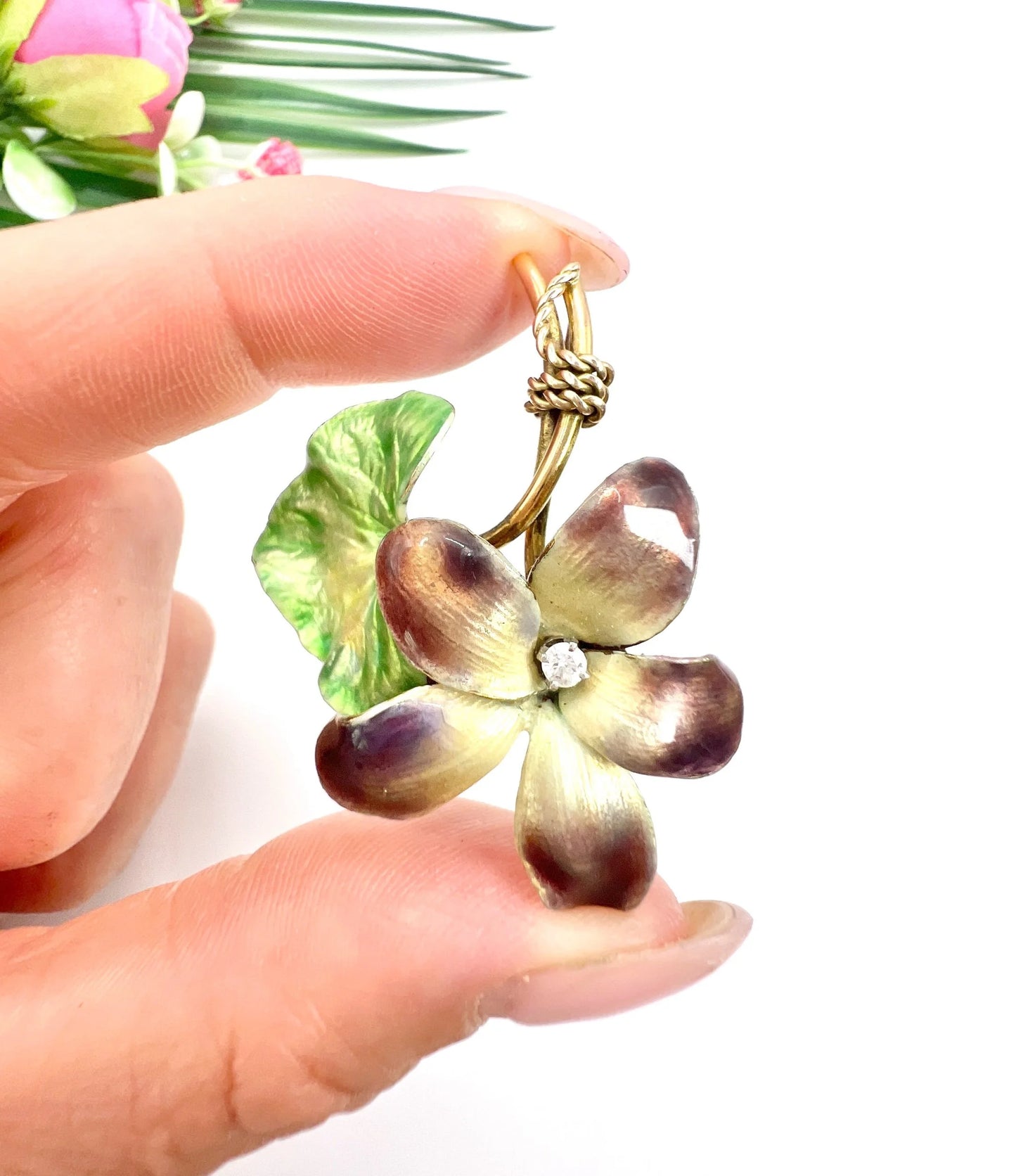 A gold and enamel flower pendant with diamond, held in a hand