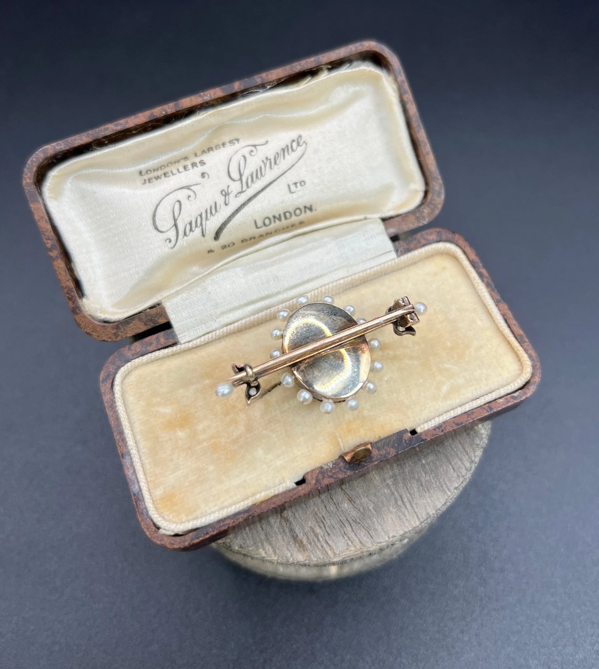 A yellow gold bar brooch with a red enamel centre surrounded by pearls, with a diamond flower motif and diamond leaves at either end, in a box