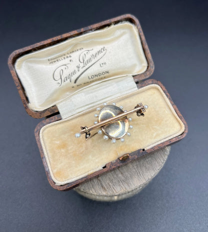 A yellow gold bar brooch with a red enamel centre surrounded by pearls, with a diamond flower motif and diamond leaves at either end, in a box