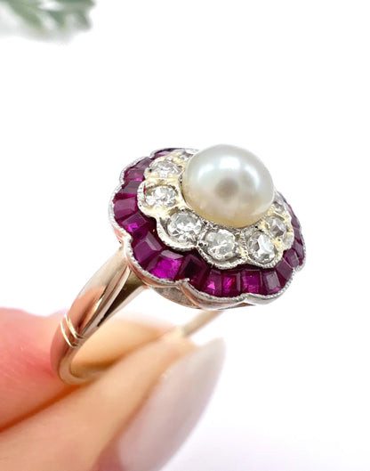 A pearl, diamond and ruby fancy cluster ring in platinum and yellow gold, held in a hand