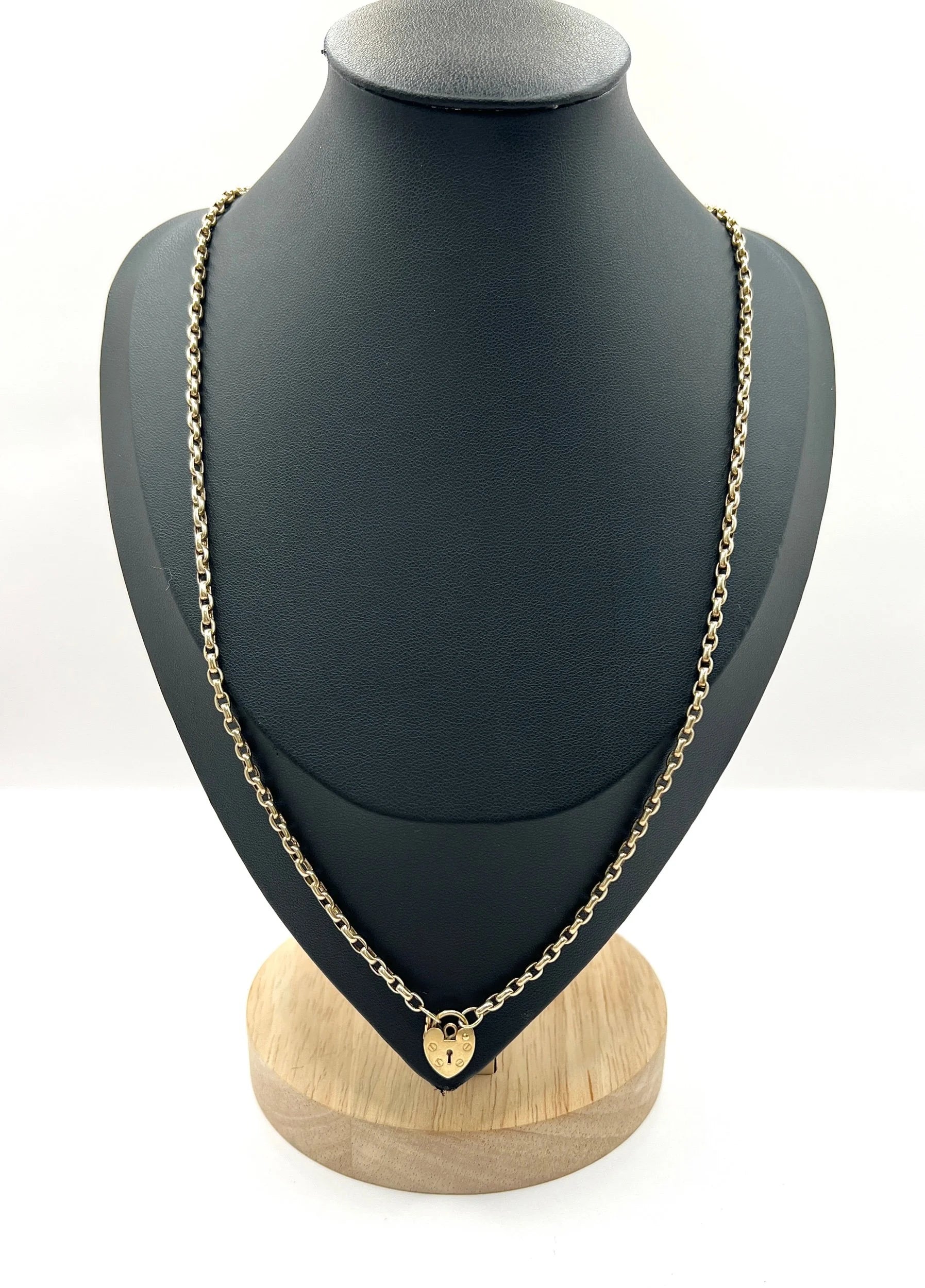 A gold belcher link chain with a heart shaped padlock clasp pendant, on a black jewellery bust