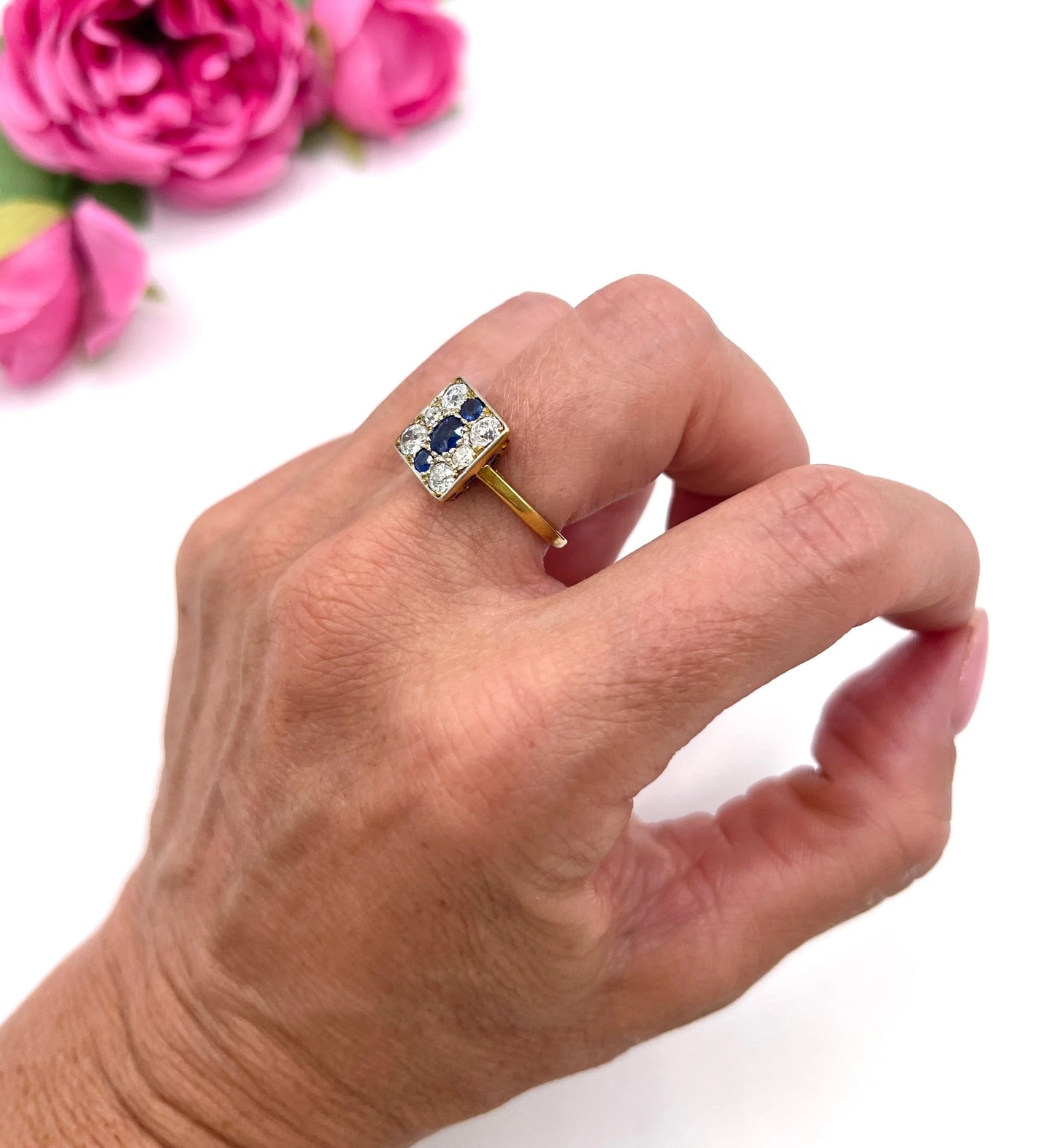 A square-shaped cluster ring with sapphires and diamonds in yellow gold and platinum, modelled on a hand