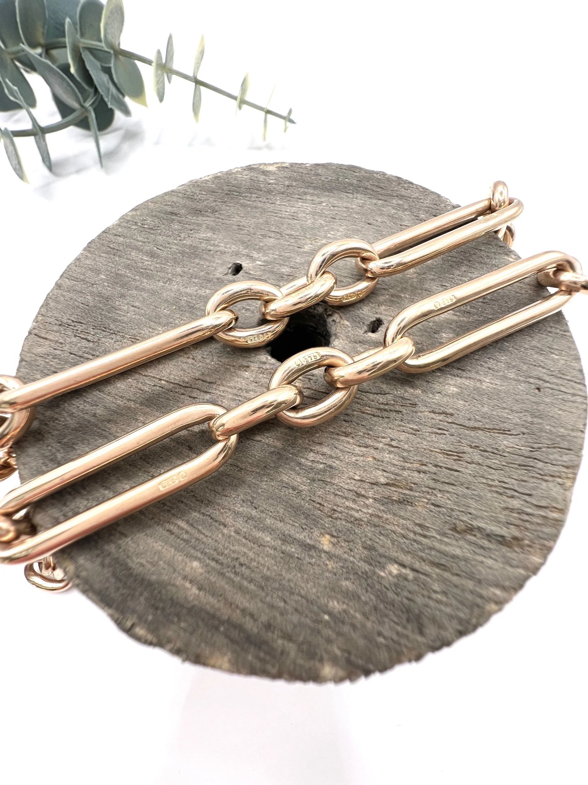 A rose gold trombone and fetter link Albert chain lying on top of a wooden object, on a white background