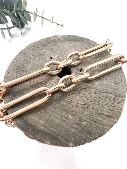 A rose gold trombone and fetter link Albert chain lying on top of a wooden object, on a white background