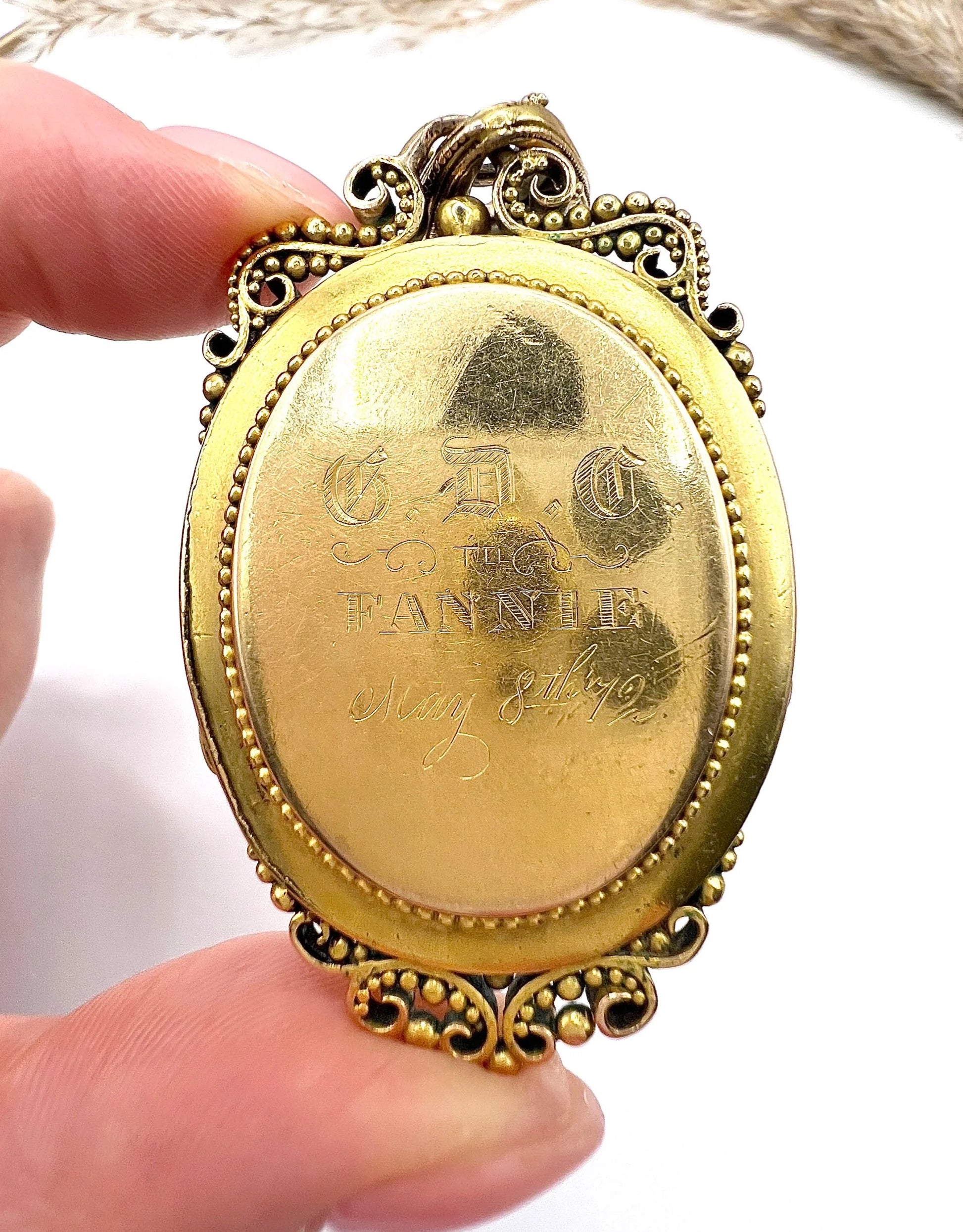 A close-up of engraving on an ornate yellow gold pendant held in a hand