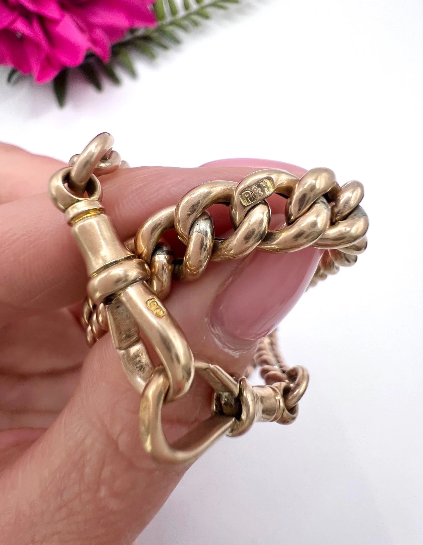 A rose gold curb link Albert chain with t-bar, held in a hand, showing a maker's mark