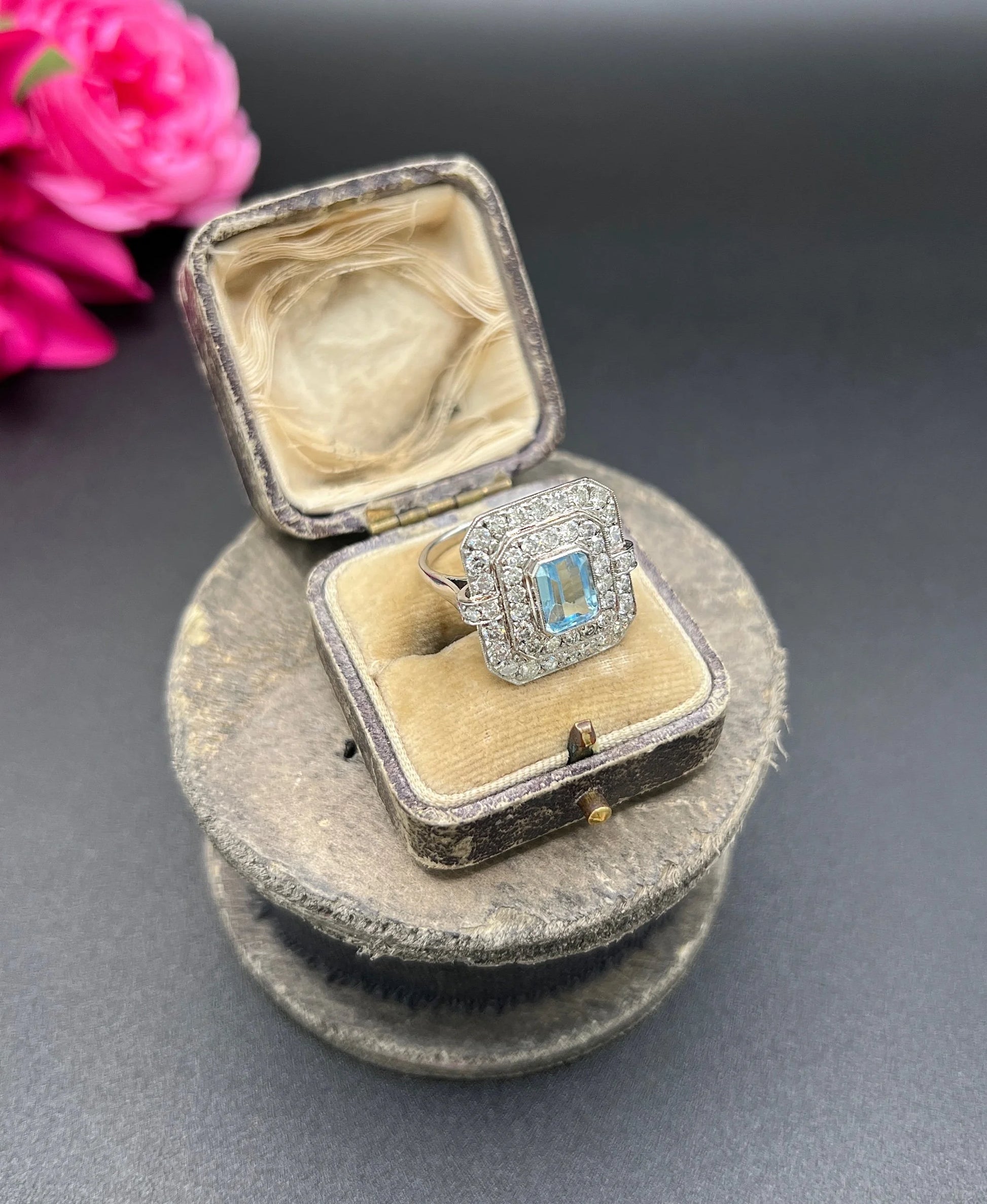 An octagonal shaped cluster ring with an aquamarine centre surrounded by two rows of diamonds, in platinum, in a ring box