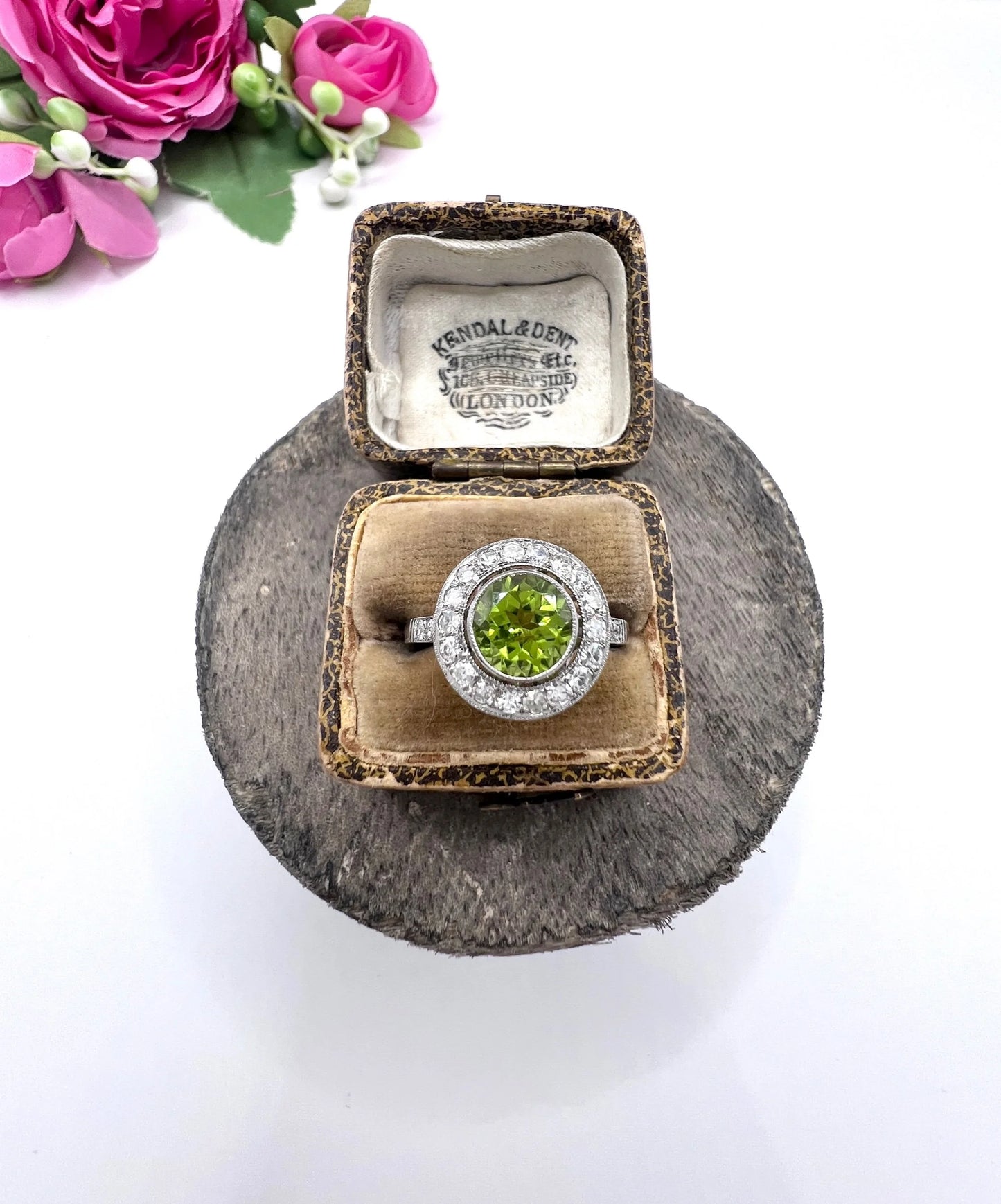 A white gold circular target cluster ring with a peridot centre surrounded by diamonds, in a ring box
