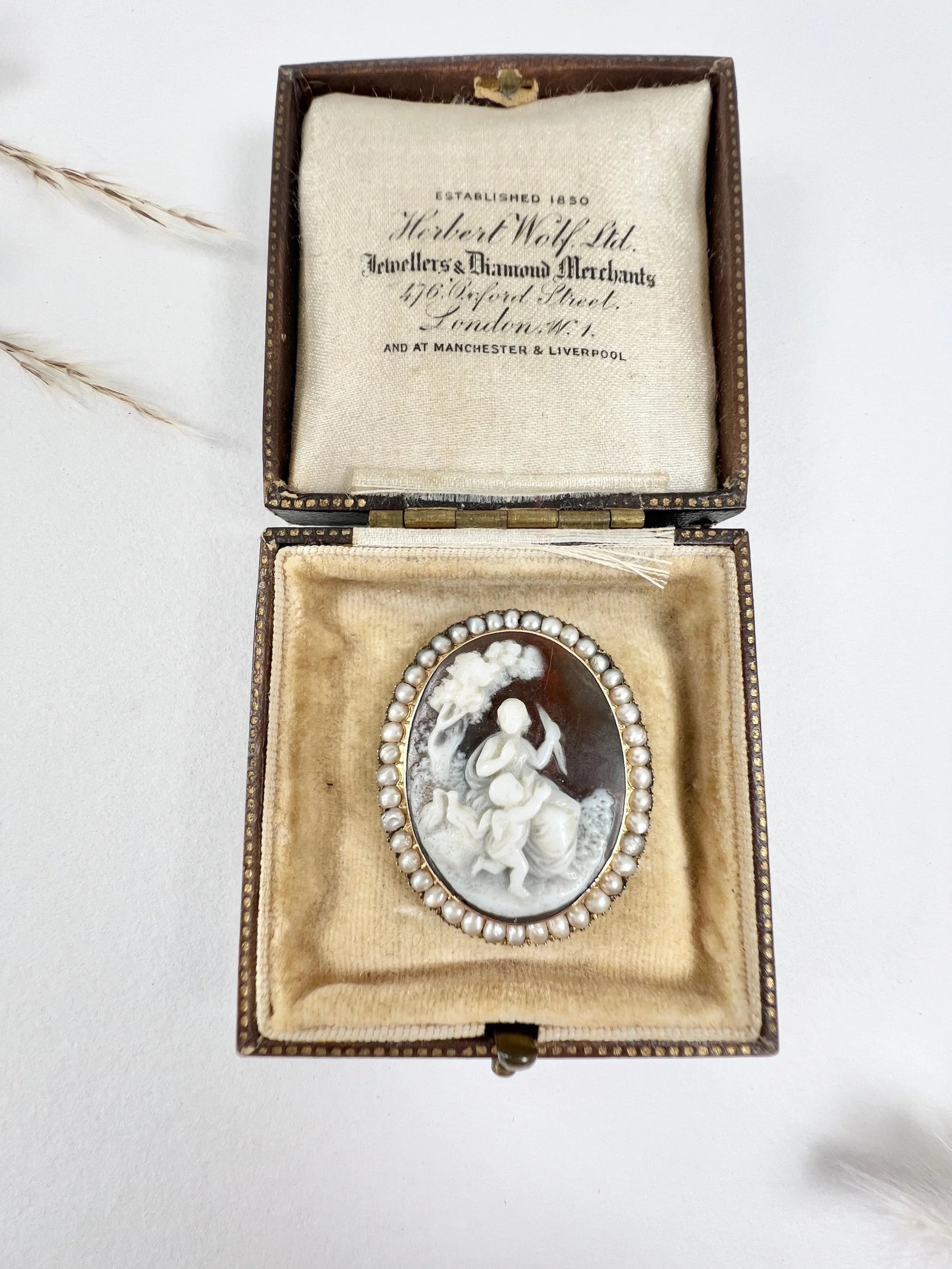 An antique oval cameo brooch depicting cherubs and birds, with a pearl border, set in gold