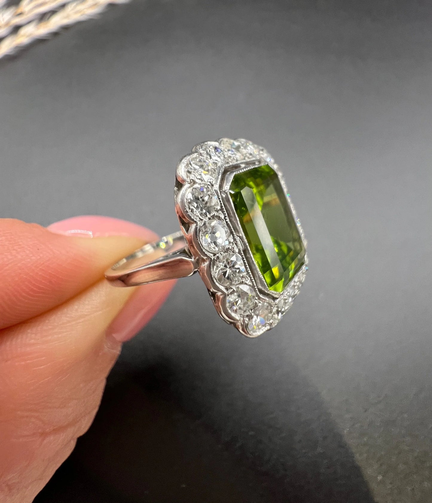 A cushion shaped peridot and diamond cluster ring in white metal, held in a hand