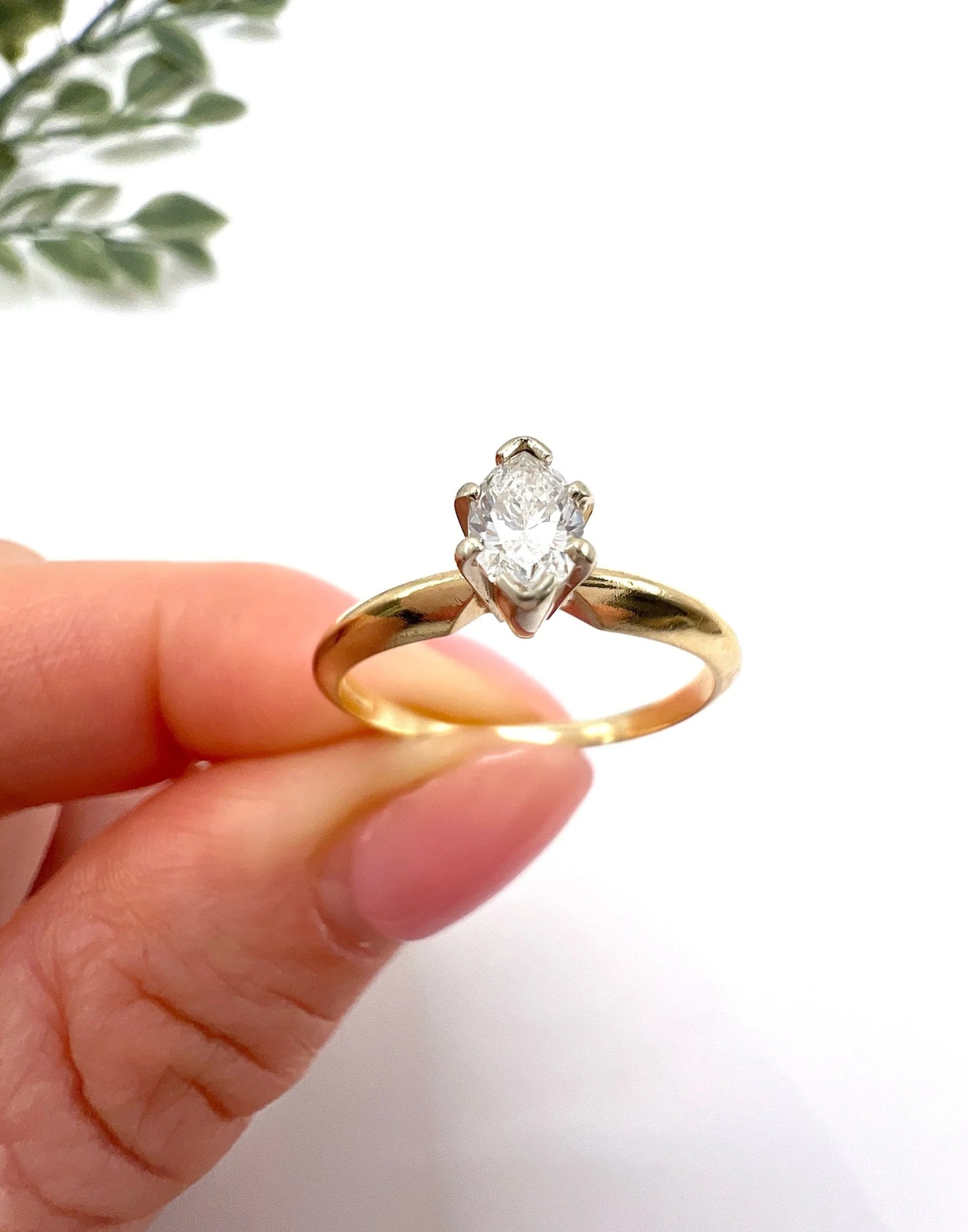A marquise diamond solitaire ring in yellow and white gold, held in a hand