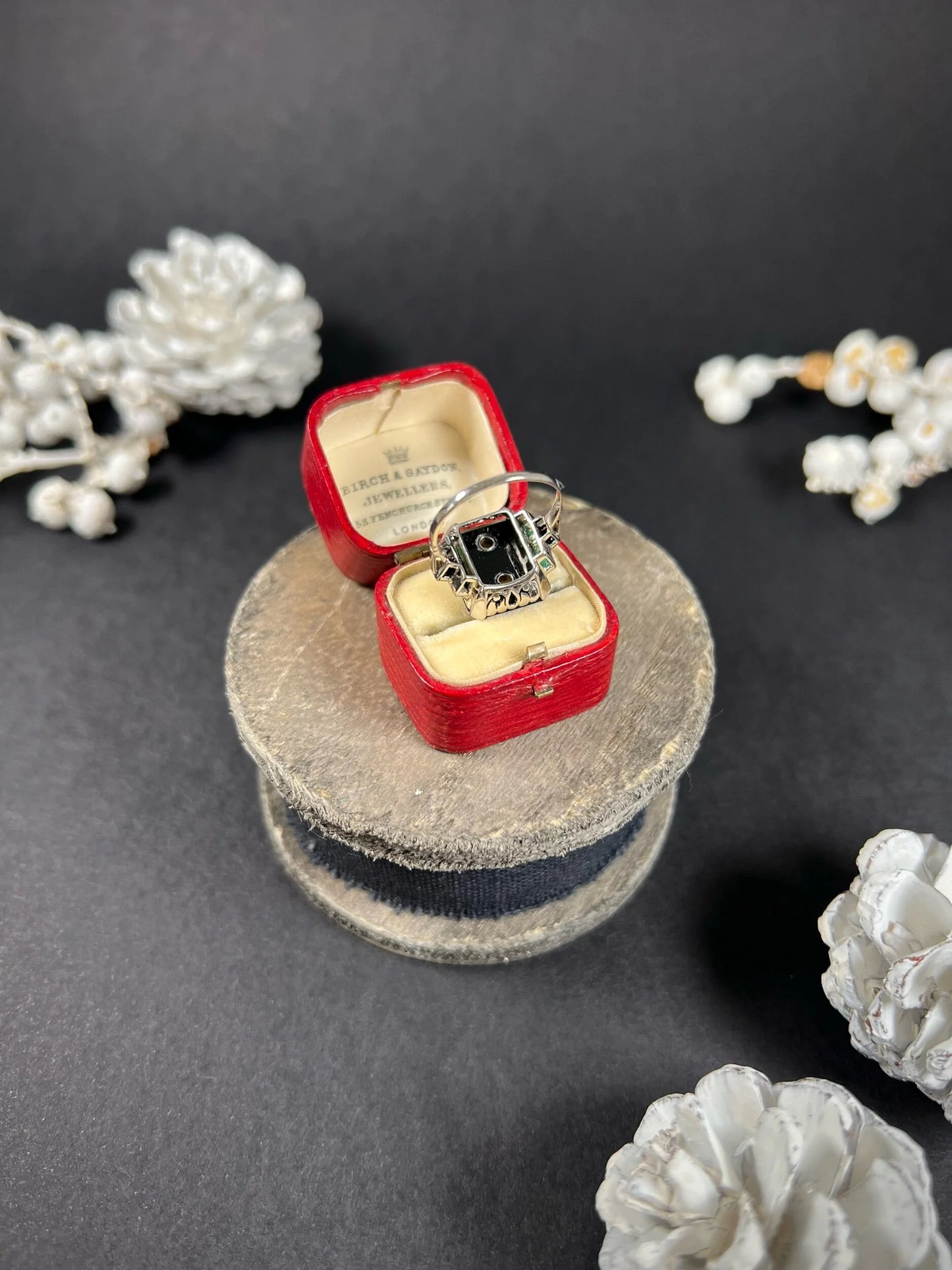 A geometric black onyx ring with diamonds and emeralds in white gold, in an antique ring box