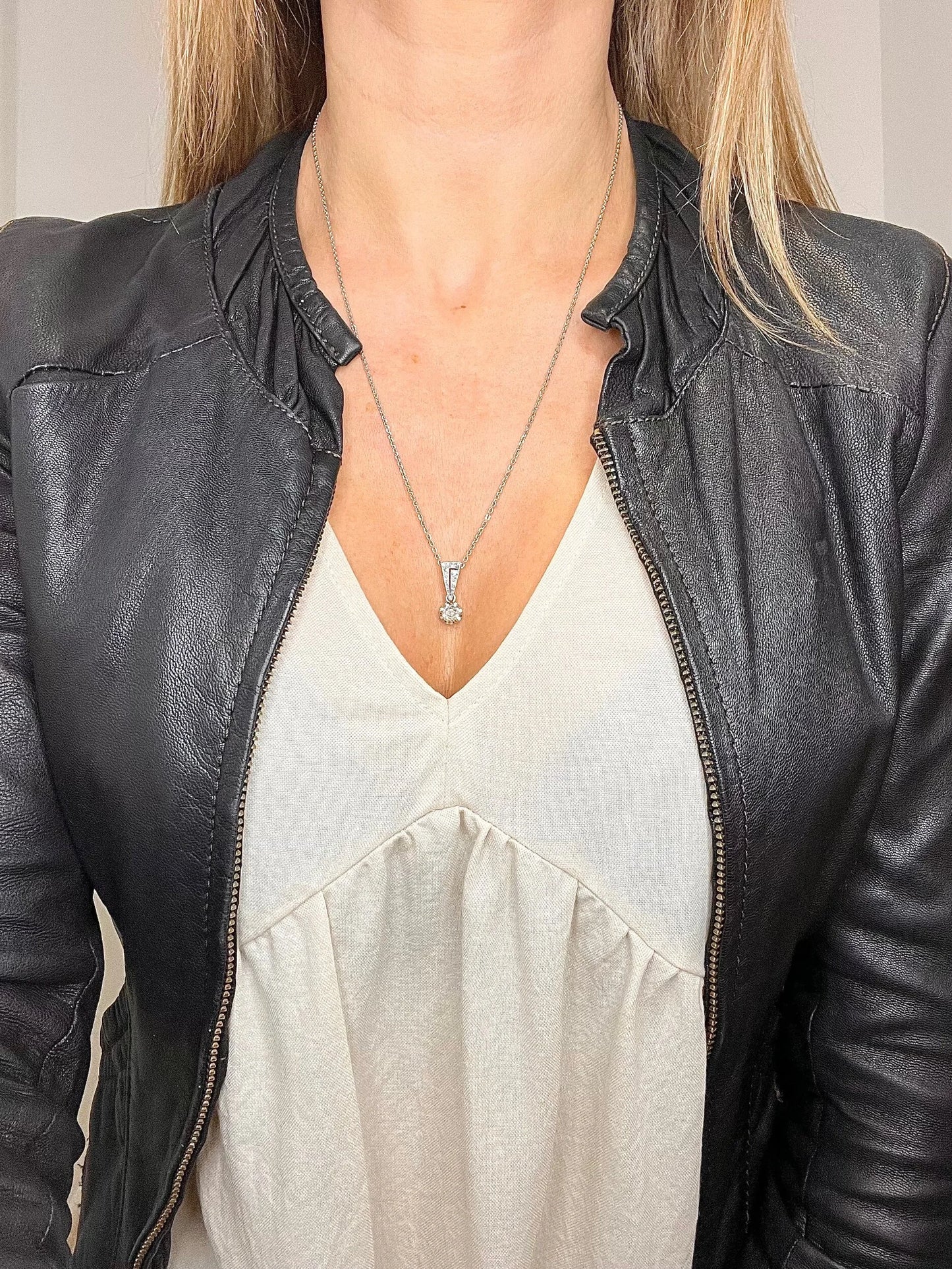 An old cut diamond pendant in white metal with a matching chain, modelled by a woman wearing a white top and black jacket