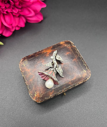 A pink enamel, diamond and pearl flower pendant in gold and silver, on an antique box