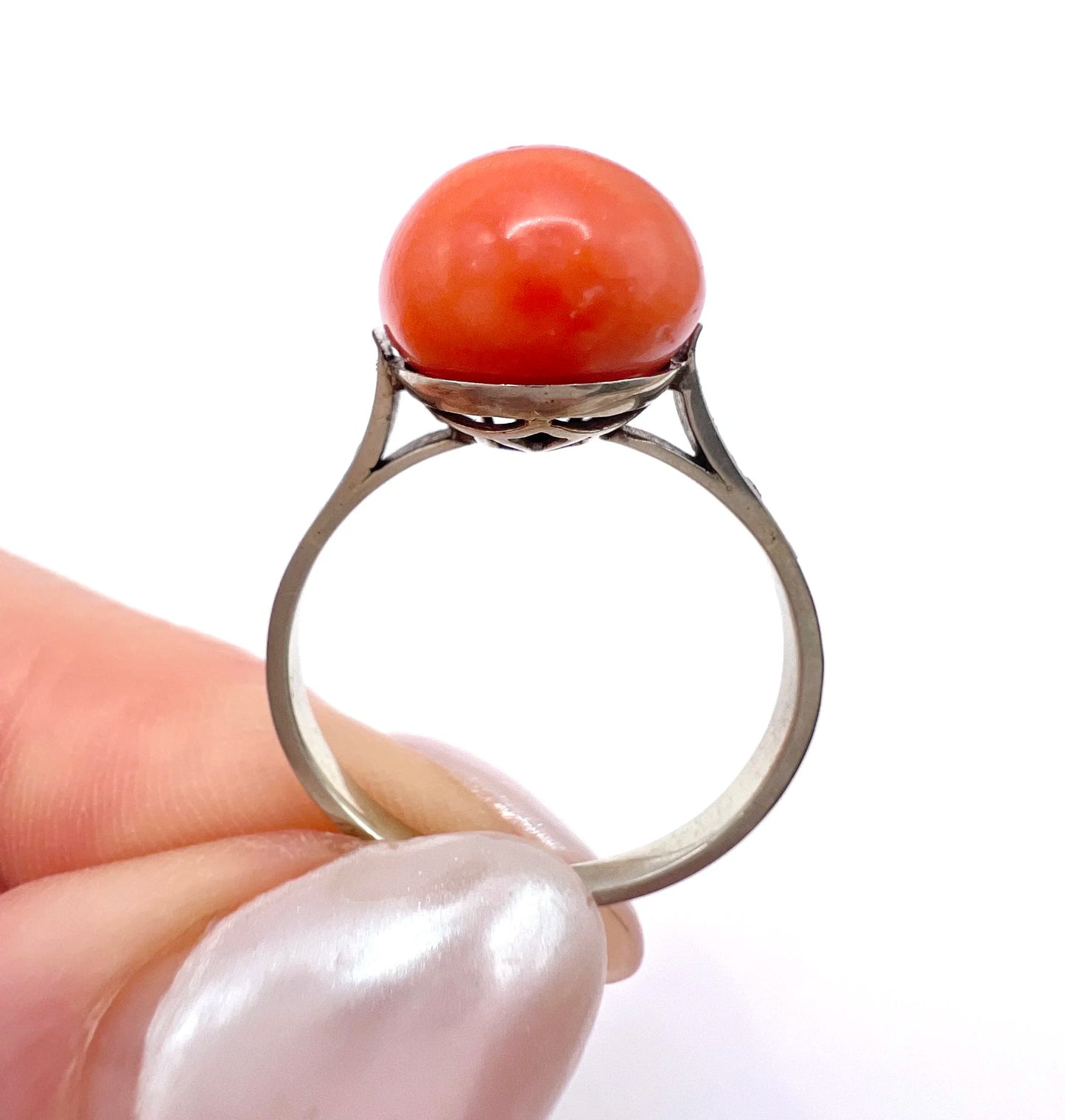A round orange coral and diamond dress ring in platinum, held in a hand