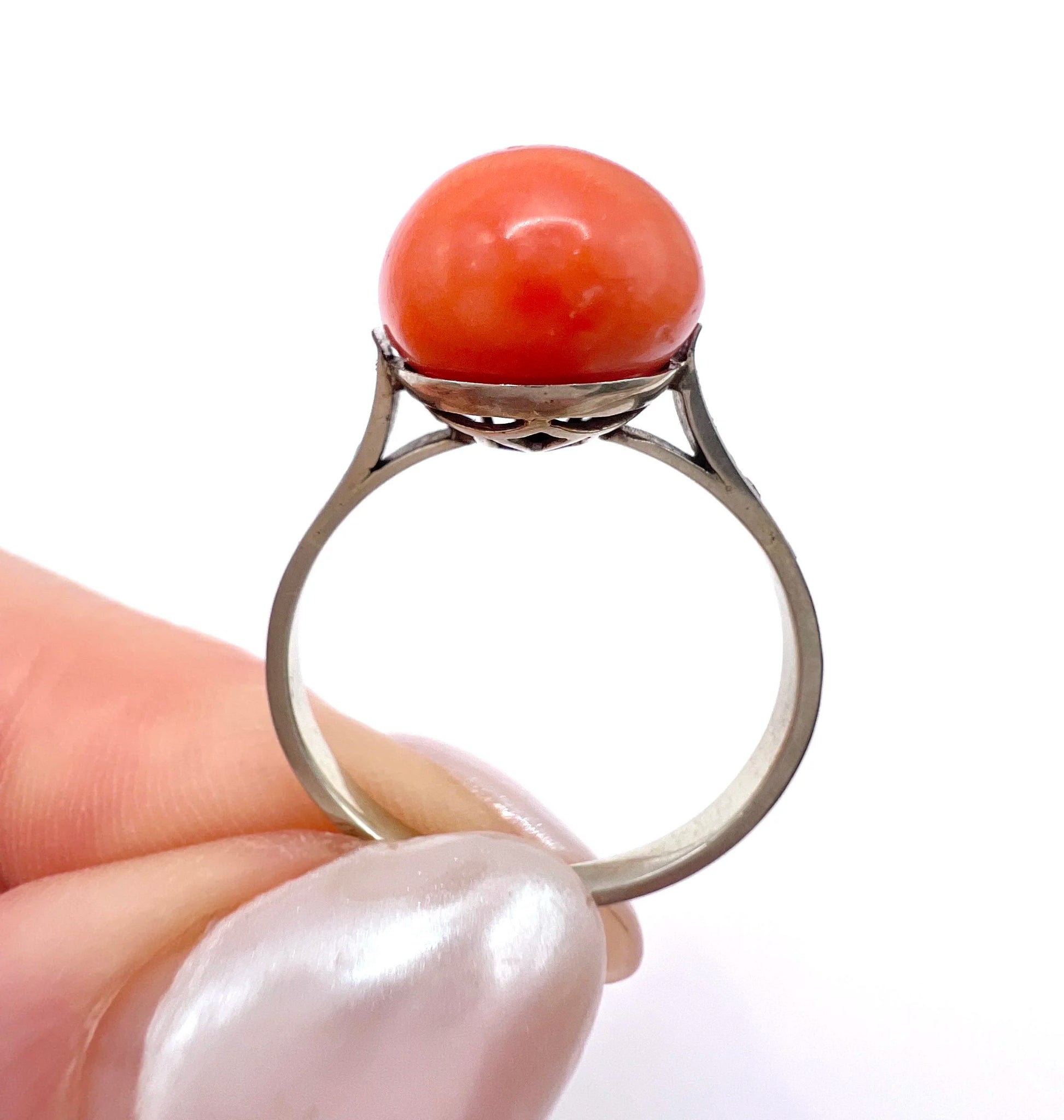 A round orange coral and diamond dress ring in platinum, held in a hand