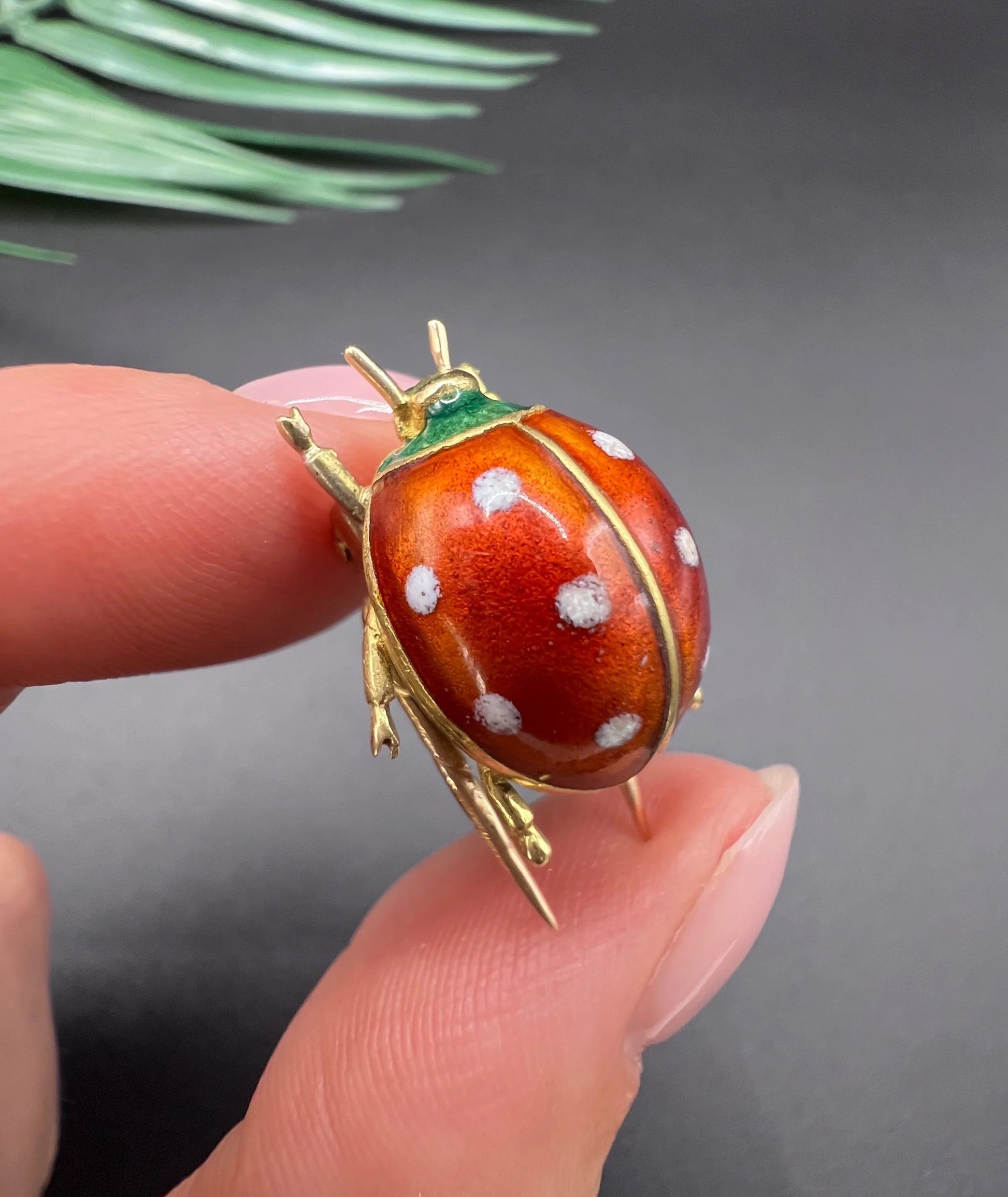 A yellow gold and enamel ladybird brooch, held in a hand