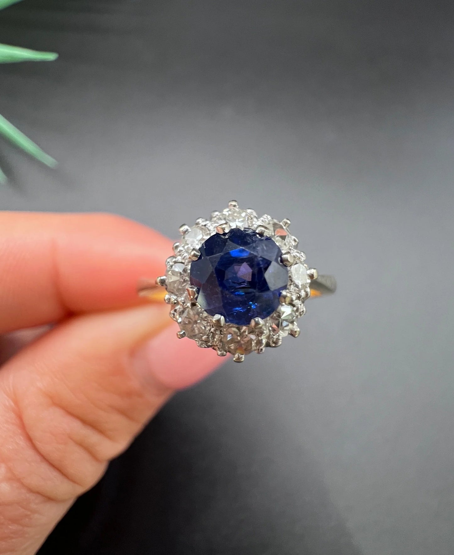 A circular cluster ring with sapphire and diamonds in yellow gold and platinum, held in a hand