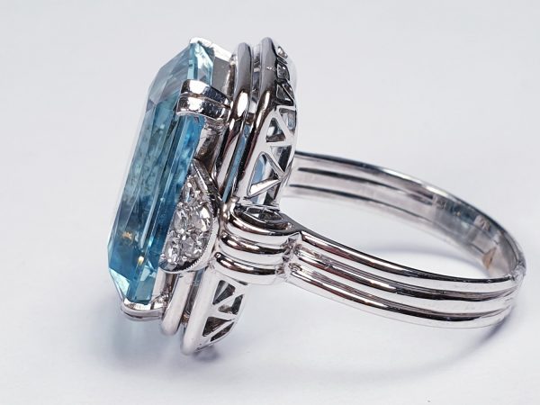 Art Deco Aquamarine and Diamond Dress Ring; a striking 14.80 carat emerald-cut aquamarine accented with half moon diamond cluster shoulders, on a three wire platinum band. Circa 1930s