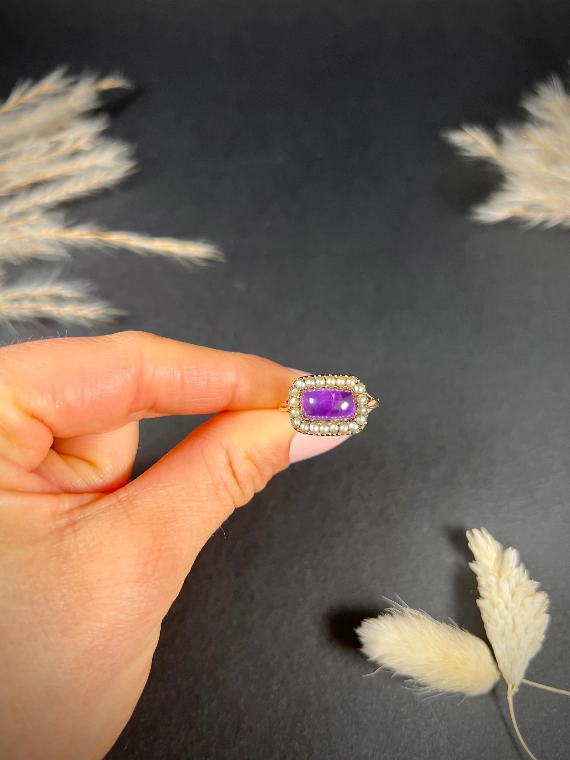 A cabochon amethyst and pearl halo cluster ring in gold, held in a hand