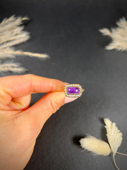 A cabochon amethyst and pearl halo cluster ring in gold, held in a hand