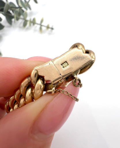 A close-up of a gold bracelet clasp stamped 15, held in a hand