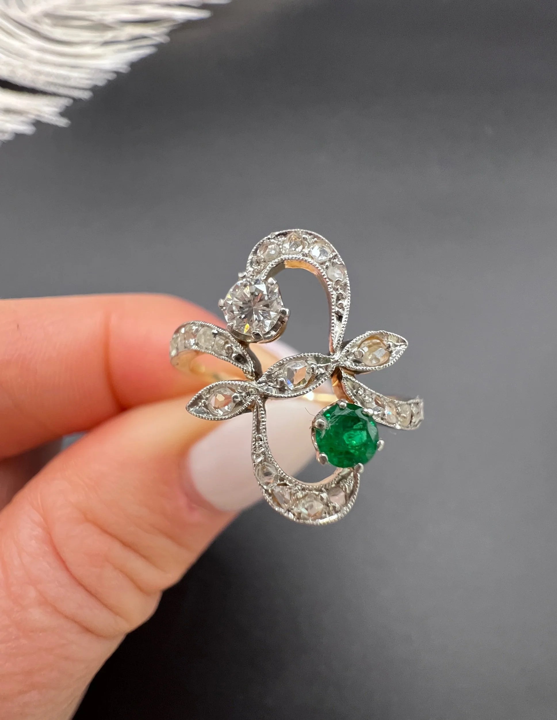 An emerald and diamond fancy openwork ring in yellow gold and platinum, held in a hand