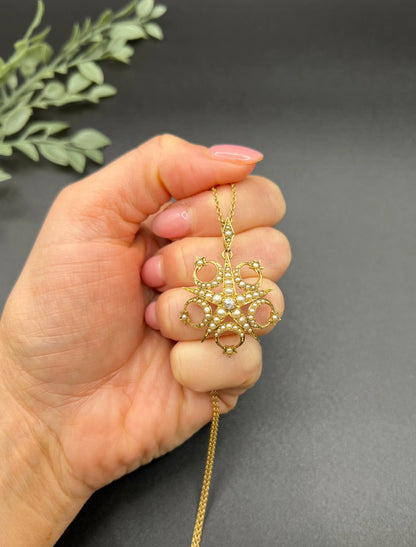 A yellow gold star and crescent brooch/pendant set with a diamond and pearls, with a gold chain, held in a hand