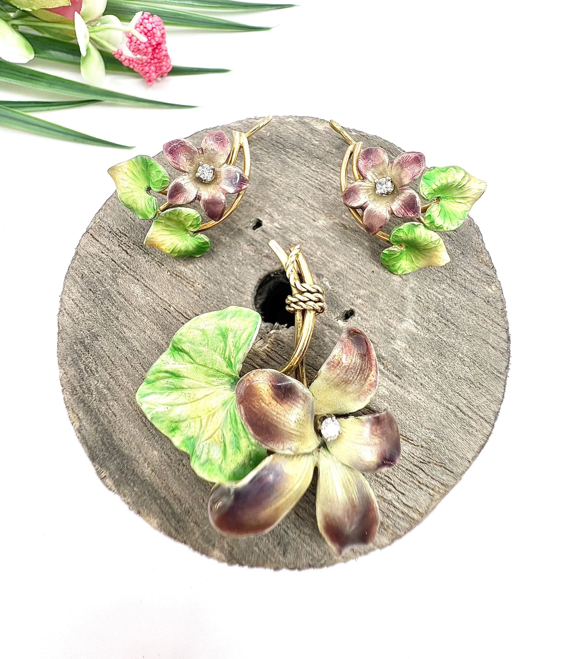 An enamelled flower suite comprising pendant and earrings, sitting on top of a wooden object