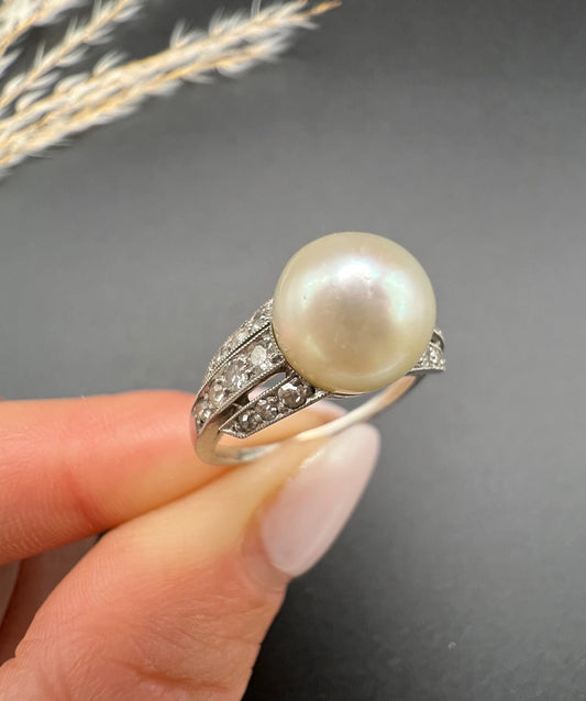 A pearl and diamond ring in platinum, held in a hand