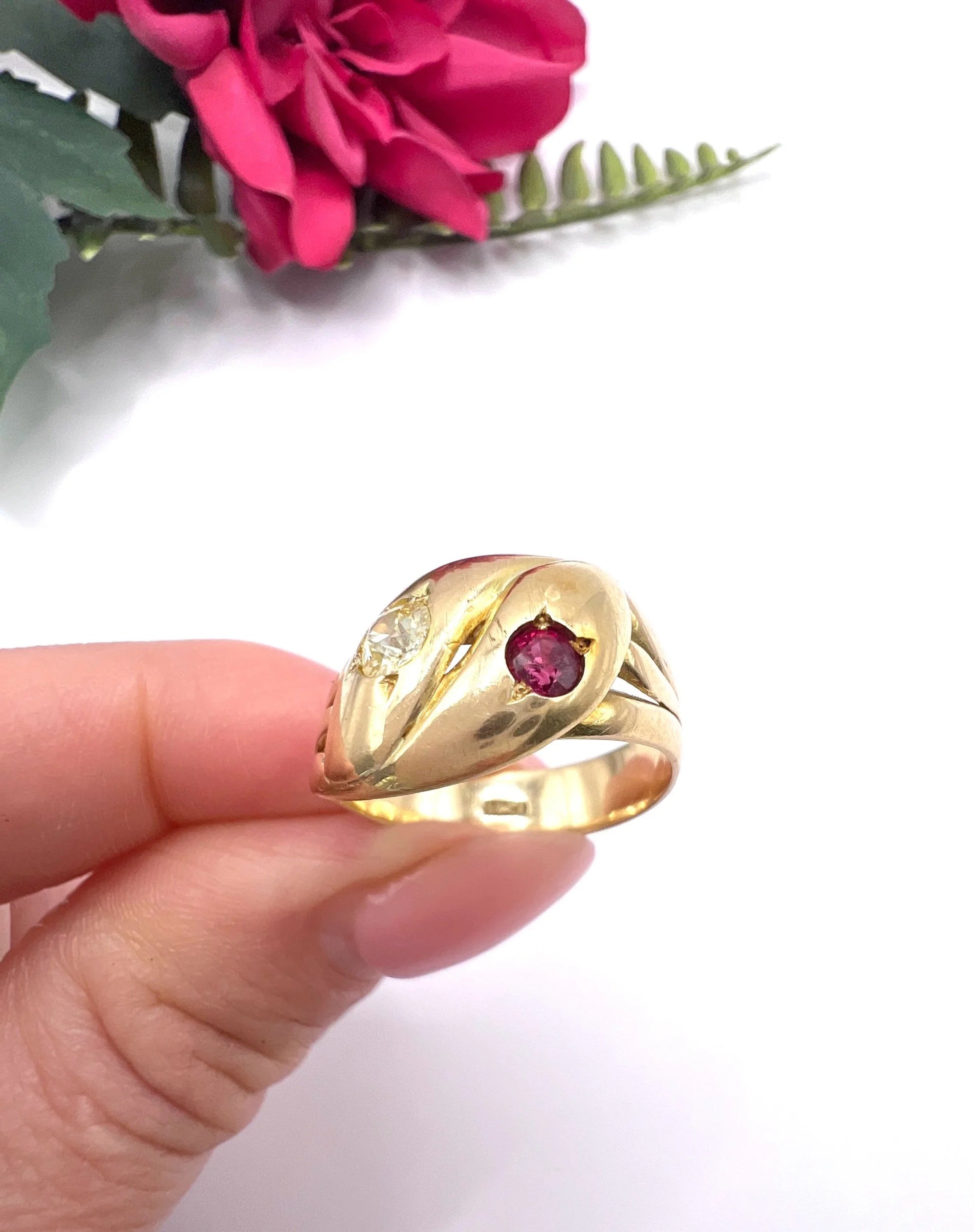 A yellow gold double headed snake ring with a ruby and a diamond, held in a hand