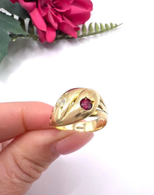 A yellow gold double headed snake ring with a ruby and a diamond, held in a hand