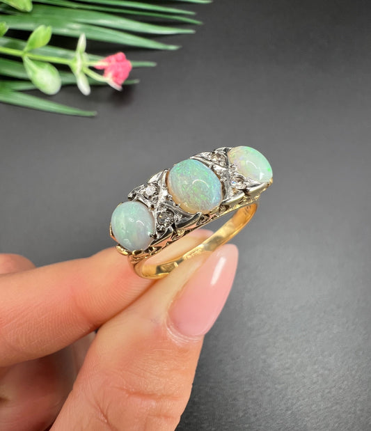 A yellow gold and platinum ring set with opals and diamonds, held in a hand