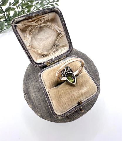 A pear cut peridot and round diamond cluster ring with bow detail, in yellow gold and white metal, in a ring box