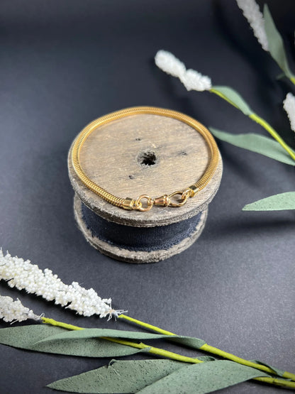A yellow gold snake link bracelet, laid on a wooden spool