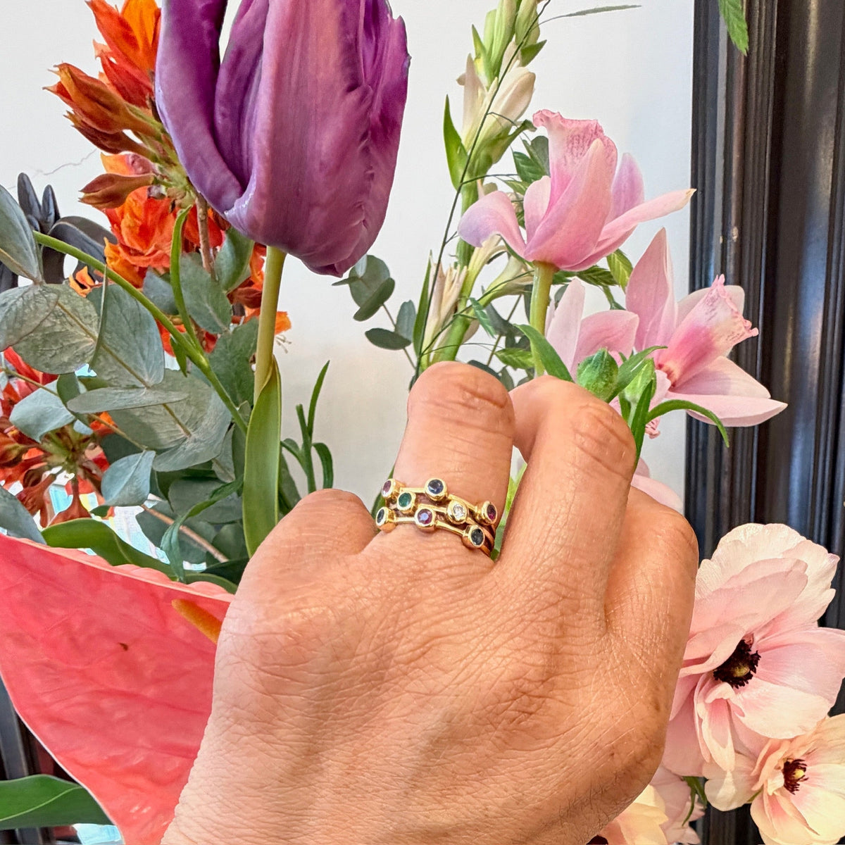 A multi-band ring in yellow gold set with round sapphires, rubies, an emerald and a diamond, modelled on a hand