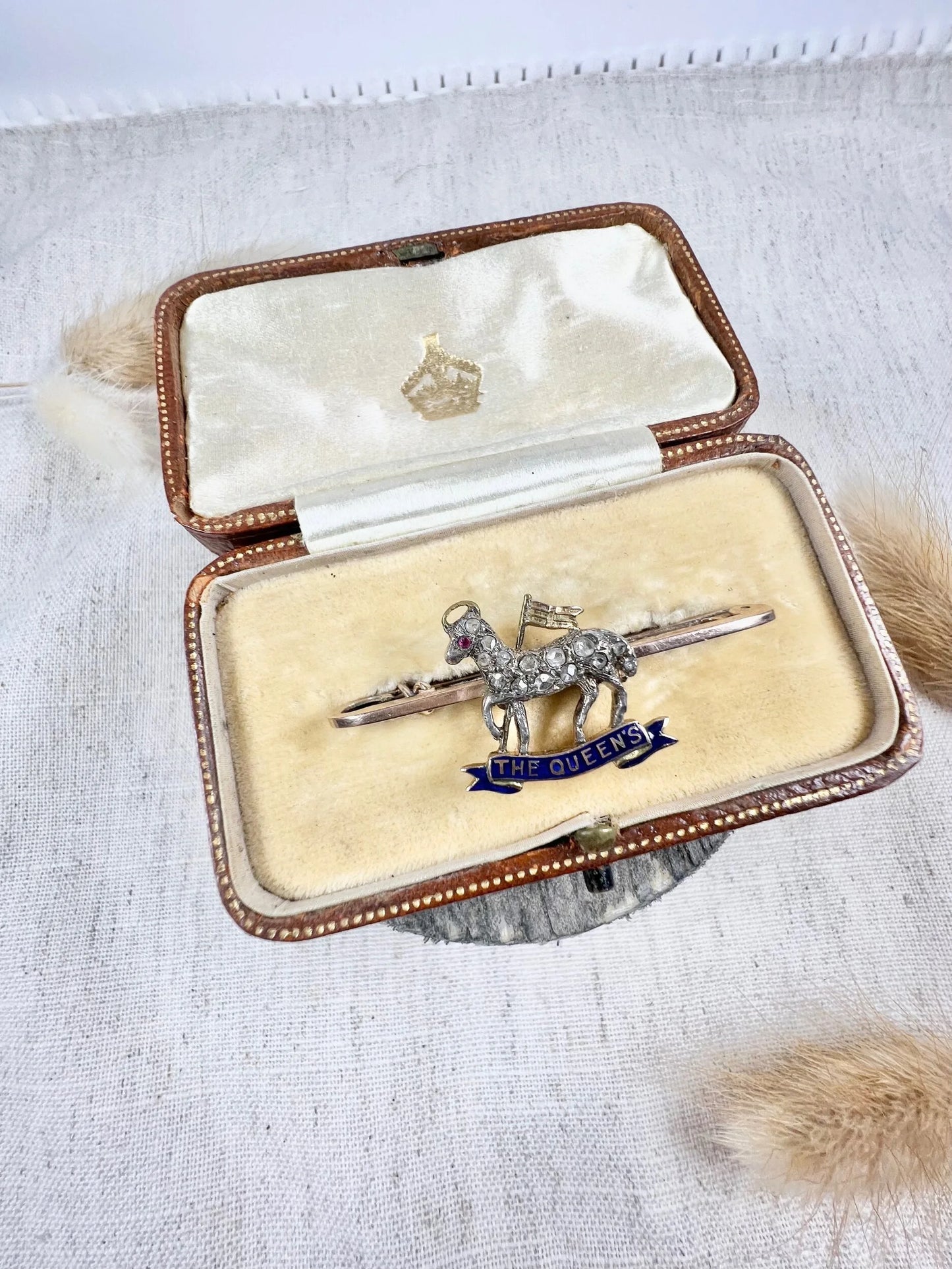 A diamond set regimental bar brooch in gold, with a blue enamel banner reading THE QUEEN'S, in an antique box