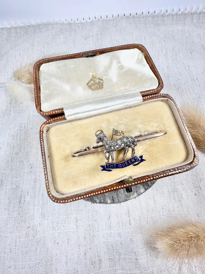 A diamond set regimental bar brooch in gold, with a blue enamel banner reading THE QUEEN'S, in an antique box