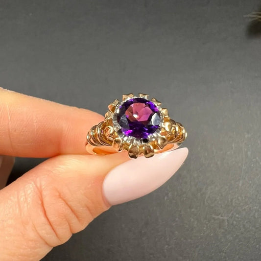A yellow and white gold single stone amethyst ring, held in a hand
