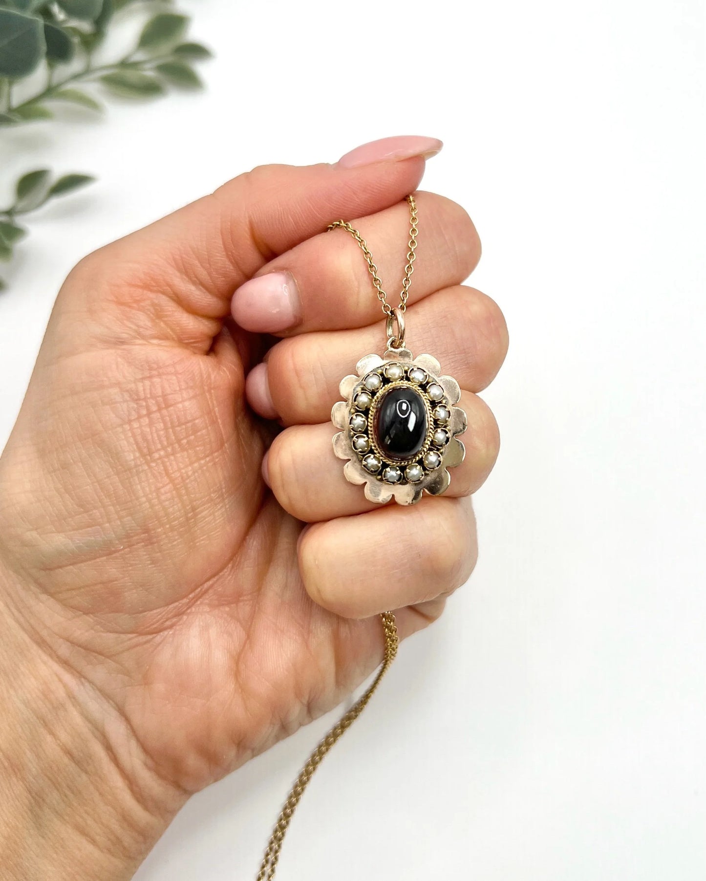 A cabochon garnet pendant with a seed pearl border in rose gold, with a chain, held in a hand
